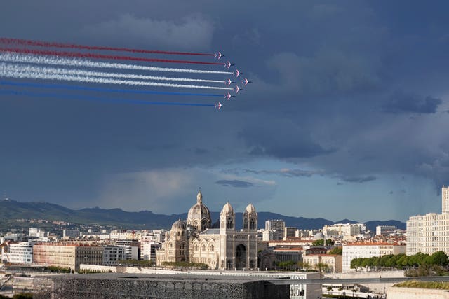 The Patrouille de France aerobatics demonstration aircraft leave a tricolor trail of smoke in the sky above La Major Cathedral as the Belem, the three-masted sailing ship bringing the Olympic flame from Greece, enters the Old Port in Marseille, southern France