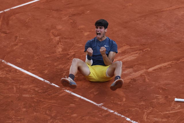 Carlos Alcaraz fist pumps while sat on the floor as he celebrates winning the French Open