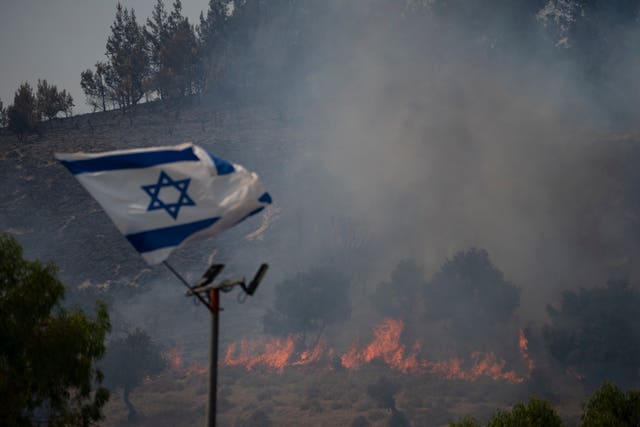Fires burn as an Israeli flag flutters among the smoke