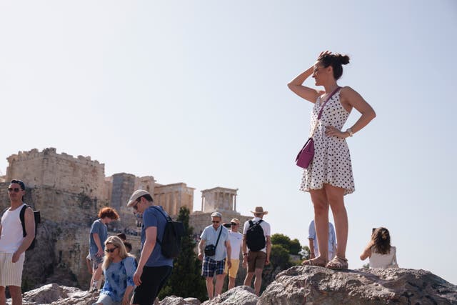 Tourists stand on a hill in front of the Acropolis in central Athens