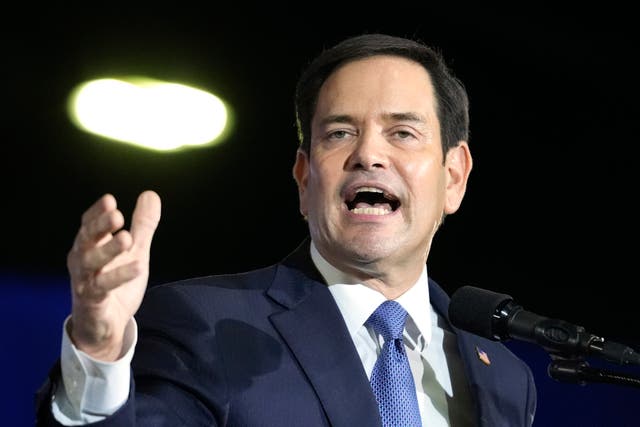 A man in a blue suit is gesturing to the camera