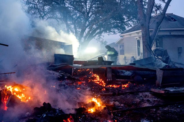 A firefighter sprays water on a burning outbuilding as the Point Fire spreads in Healdsburg, California