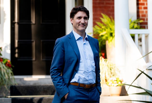 Canadian Prime Minister Justin Trudeau with his hands in his pockets and smiling while wearing a suit and an open collar shirt