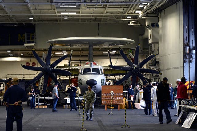 Crew members walk by aircraft in the hangar of the Theodore Roosevelt (CVN 71), a nuclear-powered aircraft carrier, anchored in Busan Naval Base in Busan, South Korea