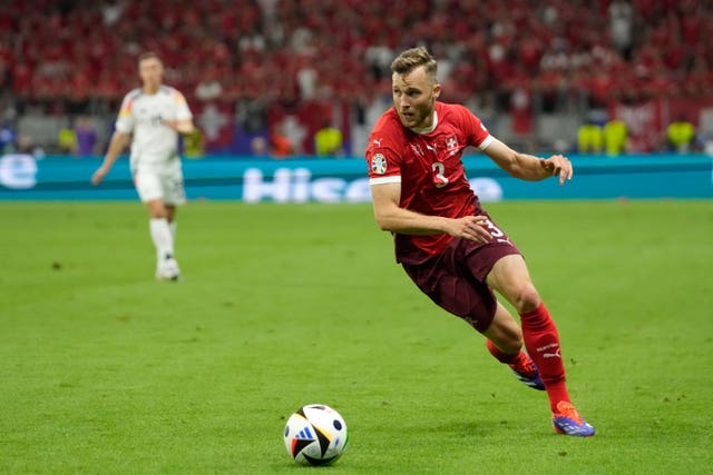 Switzerland’s Silvan Widmer, wearing an all-red uniform, chases after a ball in the foreground