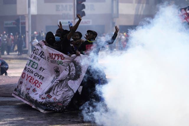Protesters hide behind a banner as police fire tear gas at them during a protest over proposed tax hikes in a finance Bill in Nairobi, Kenya