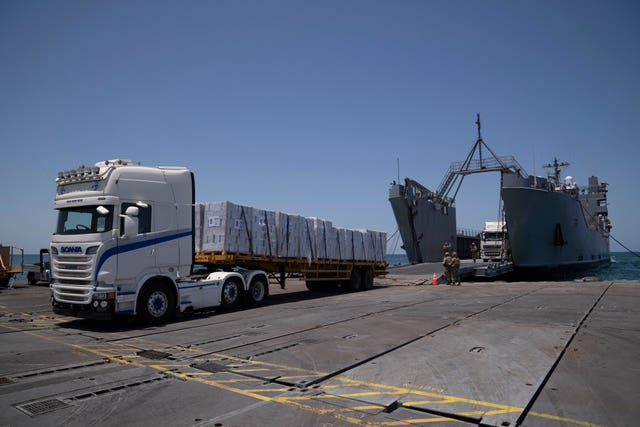 US Army soldiers stand next to trucks arriving loaded with humanitarian aid at the US-built floating pier in Gaza