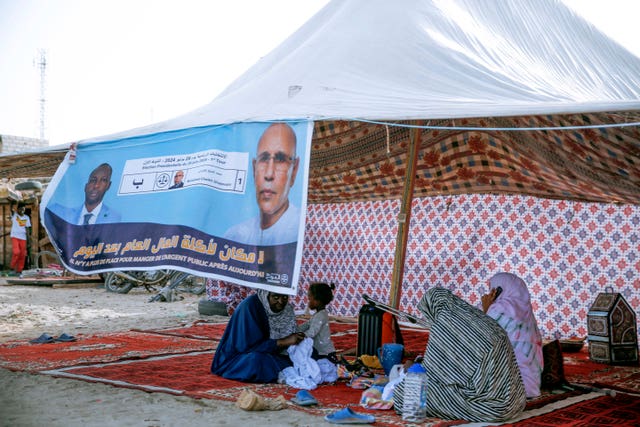 Women sit behind an electoral banner for Mauritanian president Mohamed Ould Ghazouani