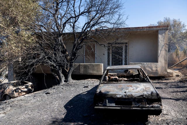 A burnt car in the garden of a house with blackened trees 