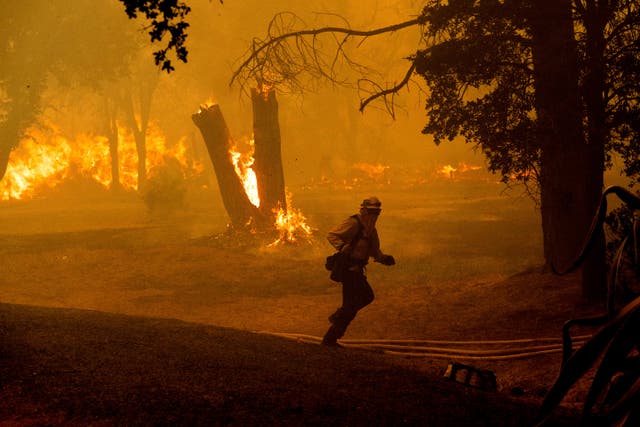 A firefighter runs through smoke filled forest, fire burns in the background