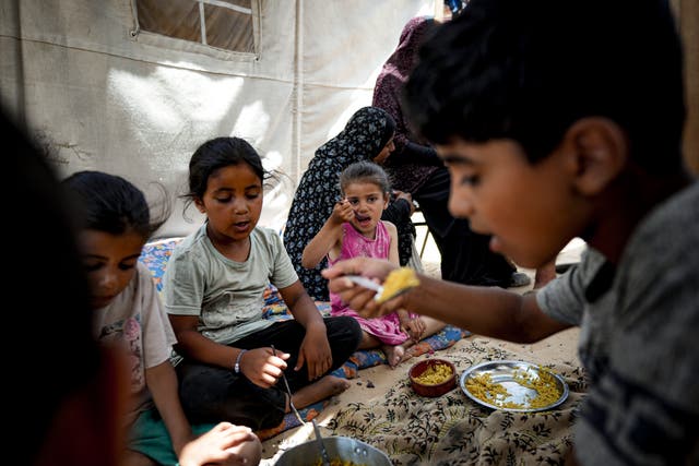 Members of the Al-Ashqar family, who were displaced by the Israeli bombardment of the Gaza Strip, eat lunch at a makeshift tent camp