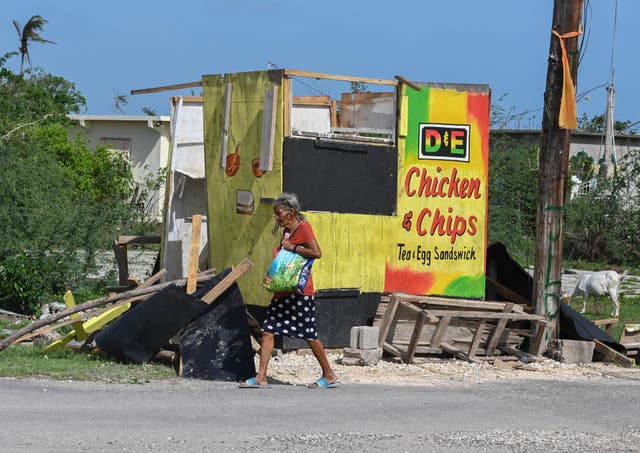 A woman walks past a food stall destroyed by Hurricane Beryl in the fishing settlement of Rocky Point, Clarendon, Jamaica