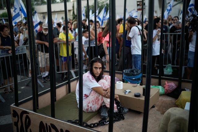A woman sits in a cage during a protest marking nine months since the start of the war and calling for the release of hostages