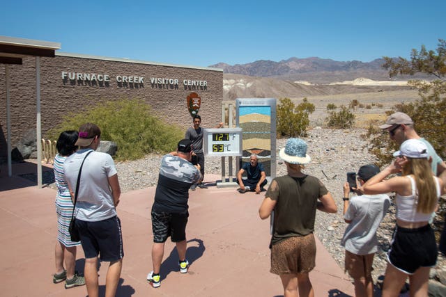 Tourists take photos in front of the Furnace Creek visitor centre thermometer 