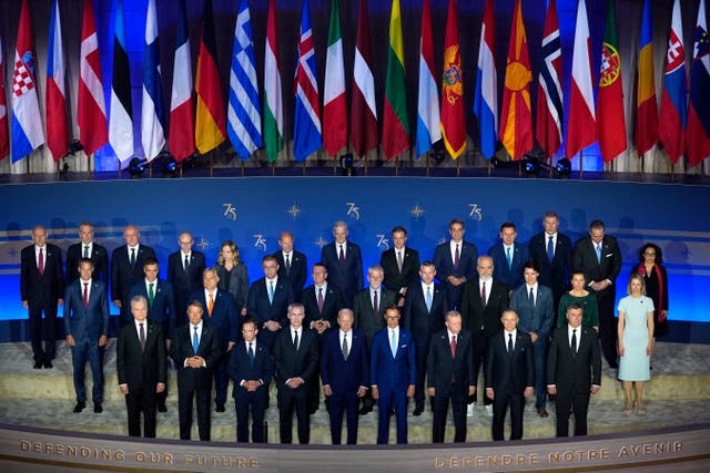 Leaders of many of the Nato nations stand together in front of their flags for an official portrait 