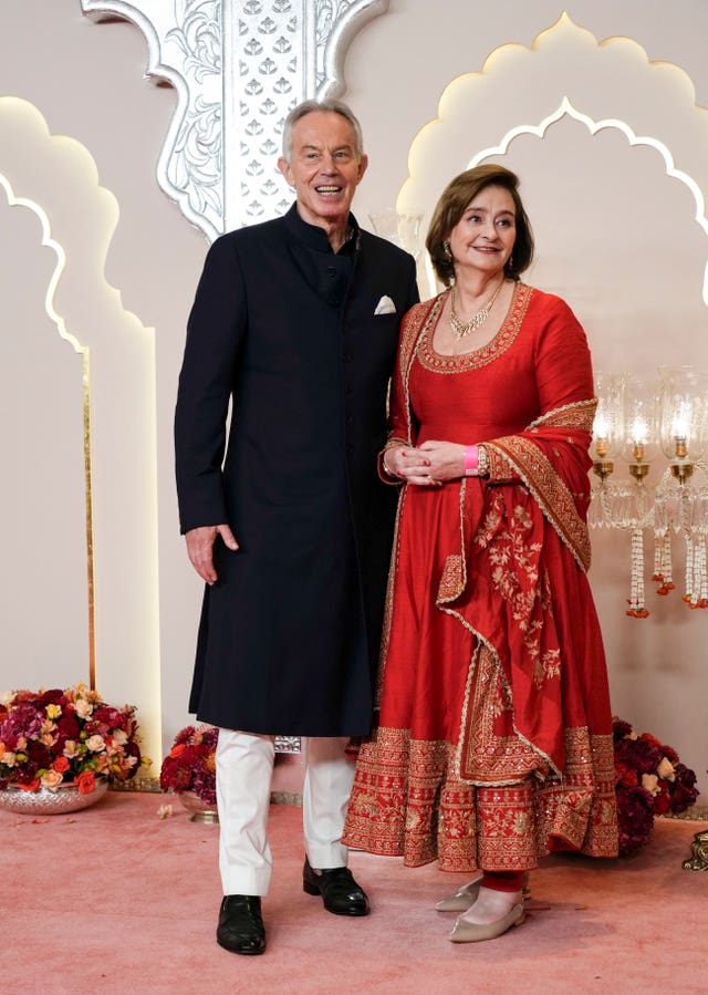 Tony Blair wearing a black suit and his wife Cherie wearing red