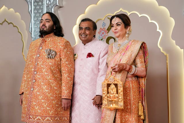 Mukesh Ambani, wearing pink, with his son Anant, wearing orange and wife Nita, wearing orange