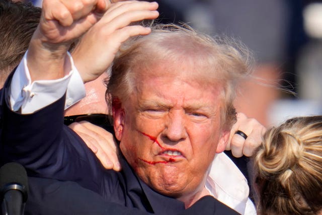 Close up of Donald Trump's face, there's blood across his lip, cheek and ear. His fist is in the air