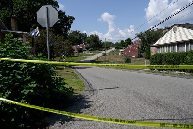 Police tape is stretched across the road in the background of the house.