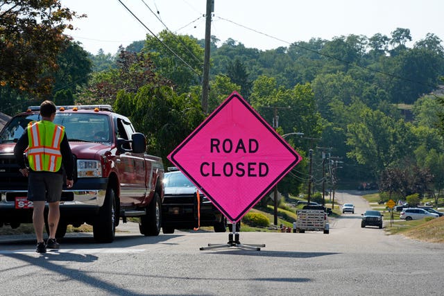 A pink road closed sign on a road with forest in the background