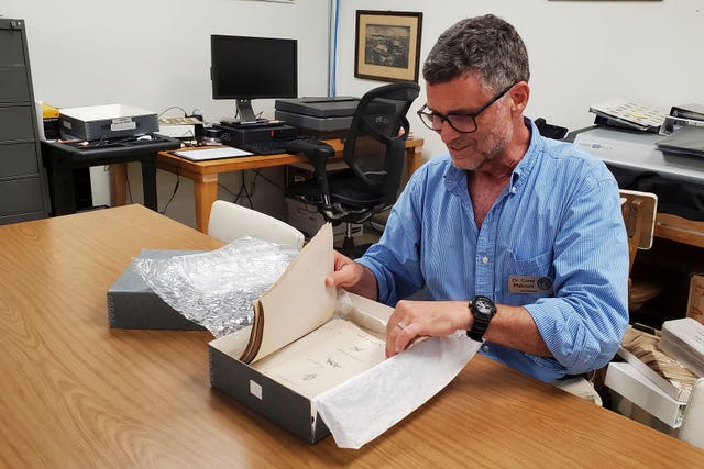 Man sitting at a desk looking through a box of papers