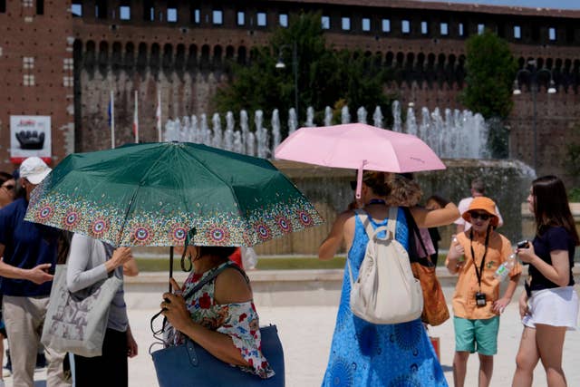 Tourists shelter from the sun in front of Sforzesco Castle in Milan, Italy