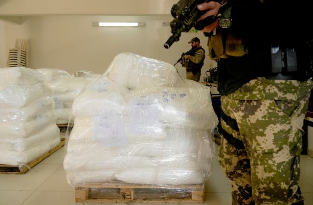 An officer with a gun guards a pile of cocaine