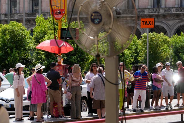 Tourists try to find some shade as they wait for a bus in Milan