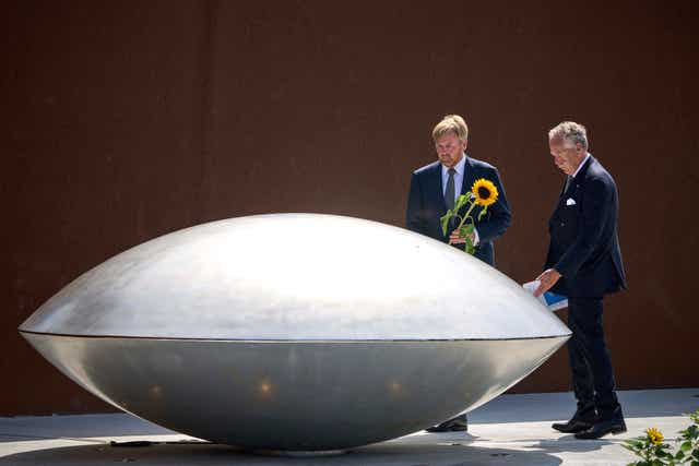 Two people stand with sunflowers by a steel rugby-ball shaped memorial statue