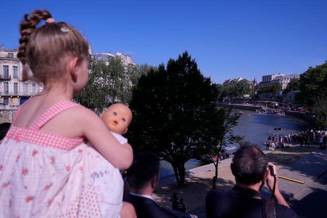 A child called Laurine holds a doll on her father Nicholas’ shoulders as she watches Paris Mayor Anne Hidalgo swimming in the Seine 