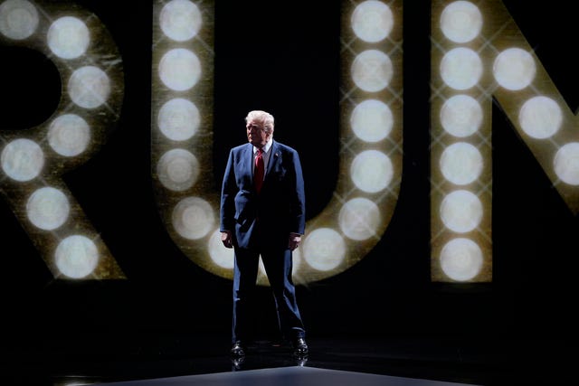 Donald Trump stands in front of 'Trump' in lights