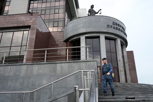 A Russian Federal Bailiffs Service employee patrols around the court building with the words reading, “Palace of justice,” on the front in Yekaterinburg, Russia