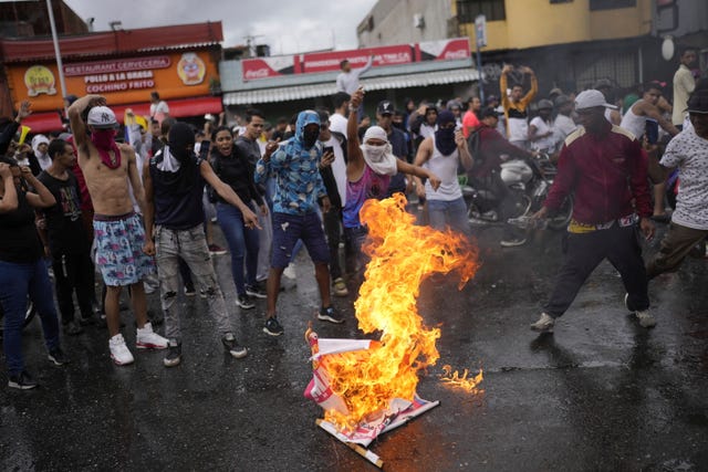 Protesters burn an election campaign poster of President Nicolas Maduro as they demonstrate against the official election results