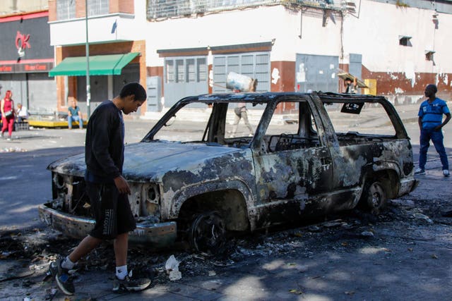 Residents stand around a vehicle burned during the previous day’s protests against official election results 