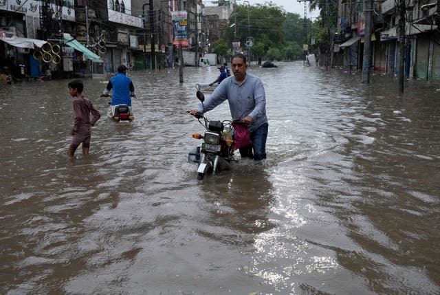 Motorcyclists riding through a flooded road caused by heavy monsoon rainfall in Lahore, Pakistan