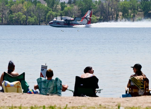 Plane skims over lake in the background, while people in sunloungers watch from the shore