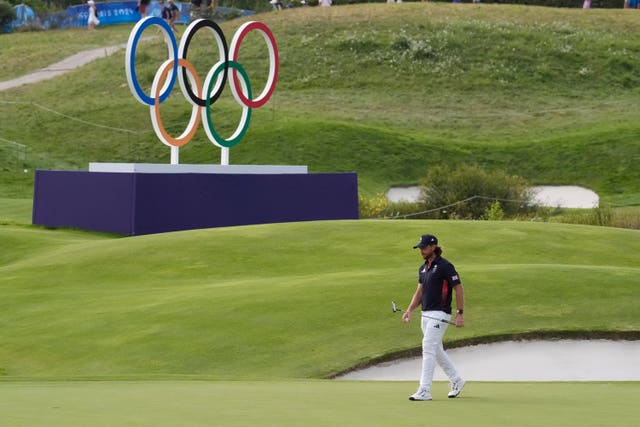 A long shot of Tommy Fleetwood, putter in hand, as he walks past the Olympic rings at Le Golf National.