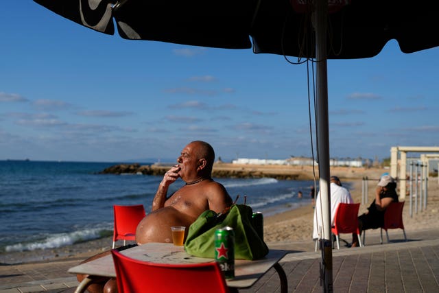 A man smokes under a beach umbrella by the sea