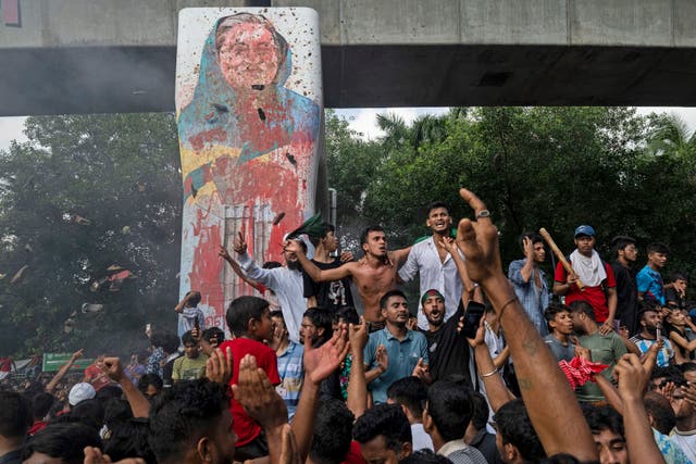 Protesters celebrate beside a defaced portrait of Prime Minister Sheikh Hasina after news of her resignation, in Dhaka, Bangladesh