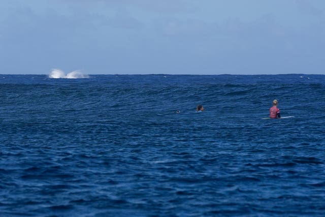 A whale, breaches as Brisa Hennessy, of Costa Rica and Tatiana Weston-Webb, of Brazil, compete during the semi-final round of the surfing competition in Tahiti