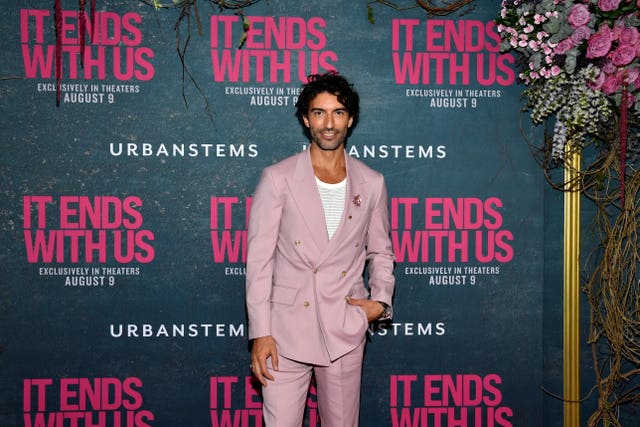 Justin Baldoni in a salmon suit in front of promotional material for It Ends With Us at the film's world premiere