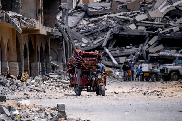 A three-wheel vehicle carries belongings away from destroyed buildings