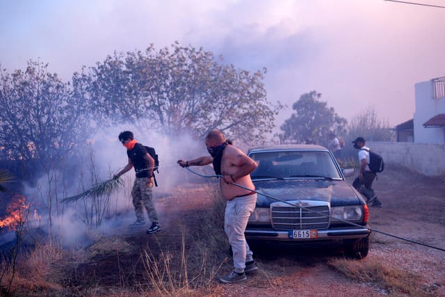 Volunteers try to extinguish the flames near a house during a fire in northern Athens 