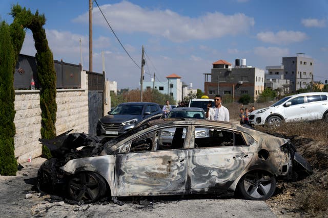 A Palestinian films a torched vehicle, seen the morning after a rampage by Israeli settlers in the West Bank village of Jit