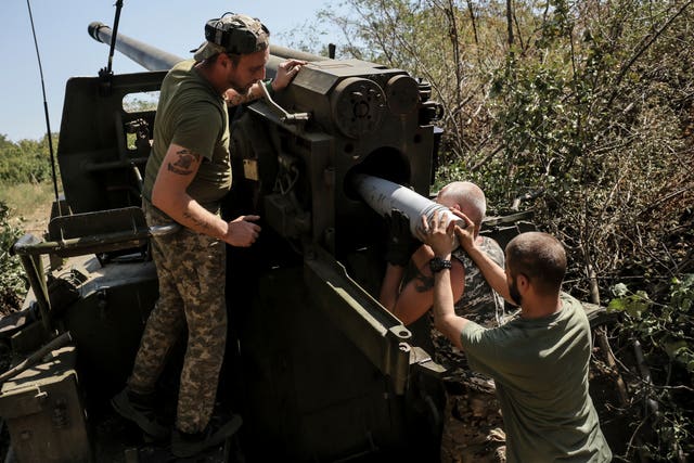 Three soldiers fire a howitzer weapon