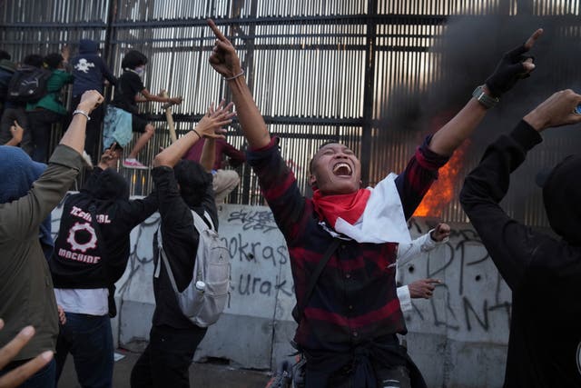 A protester in the foreground raises his arms in the air and shouts as others behind him try to scale a fence