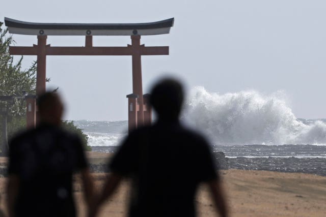 宮崎の海岸に波が打ち寄せる中、神社の鳥居の近くを歩く人々