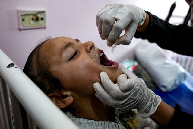 A medic in gloves administers the polio vaccine into the mouth of a girl