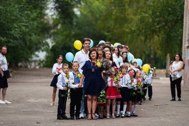 A line of school pupils, holding flowers and balloons