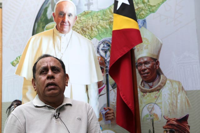 East Timor’s Minister of State Administration, Tomas Cabral, speaks to a reporter (off camera) in front of an image of the Pope.